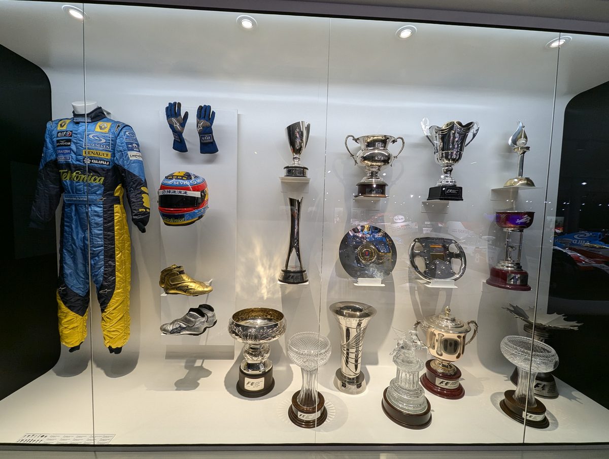 ルノー時代のレーシングスーツと優勝トロフィーが並ぶ展示ケース