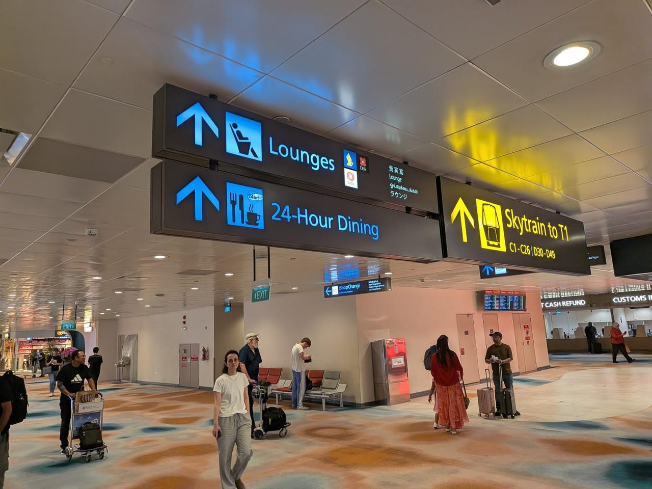 Lounges・24-Hour Dining・Skytrain to T1を示すチャンギ空港T2の天井サイン